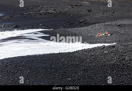 Femme en train de bronzer sur une roche volcanique noire plage, Playa Vista Papagayo, Lanzarote, îles Canaries, Espagne Banque D'Images
