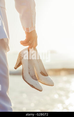 Man holding white stiletto shoes, sur une plage Banque D'Images