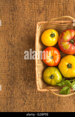 Heirloom multicolores de tomates au basilic dans un panier en osier sur une surface en bois rustique. Banque D'Images