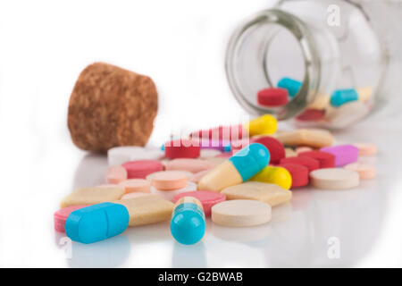 Pilules colorées close-up avec déversés par pot isolé sur fond blanc avec la réflexion Banque D'Images