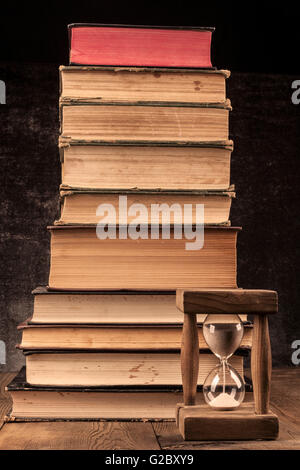 Les vieux livres de poil sur table en bois avec un fond sombre et Hourglass Banque D'Images