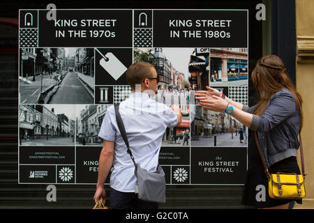Les passants à la recherche d'affichage à des images historiques de la ville. Printemps Vacances de mai dans le quartier central des affaires de Manchester affichage de photographies anciennes, photo, rétro, vintage, l'arrière-plan, photographie, appareil photo, photo, blanc, cadre, classic, illustration, résumé, bois, nostalgie, célébrer le passé, présent et avenir de la rue King. Banque D'Images