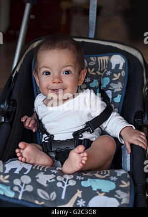 Petit bébé garçon assis dans une poussette à la maison, prêt pour une promenade dans un landau Banque D'Images