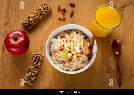 Petit-déjeuner sain : porridge d'avoine avec pomme verte, noix et baies de goji séchées, les barres granola, pomme rouge et d'orange verre Banque D'Images
