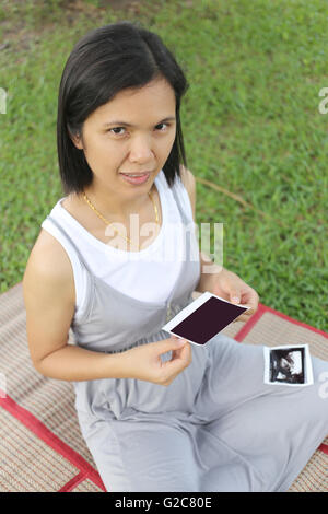 Les femmes enceintes asiatiques voir film d'échographie photo bébé sur son ventre dans la main au jardin. Banque D'Images