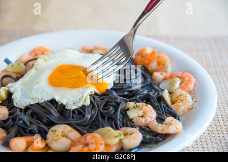 Tablier immersion dans un œuf frit sur noir spaghetti aux crevettes et l'ail. Voir de très près. Banque D'Images