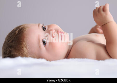 Bébé couché sur une couverture des cheveux blancs et isolé sur fond gris Banque D'Images