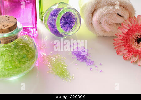 Huiles et Sels de bain sur table en verre blanc. Décorées avec des fleurs et une serviette. Composition horizontale Banque D'Images