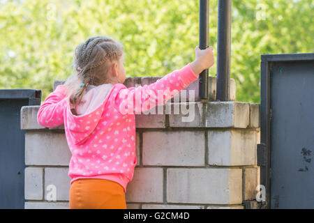 Fille de cinq ans a grimpé sur un mur de brique et attend pour lui Banque D'Images