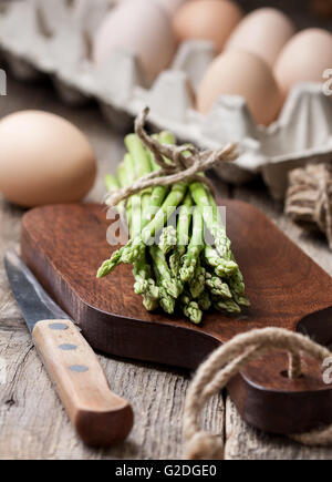 Asperges fraîches sur une planche à découper, les oeufs frais dans un panier sur un vieux fond de bois Banque D'Images