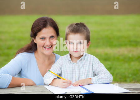 Portrait d'une femme professeur ou maman et un peu jeune garçon en chemise blanche à écrire ou à dessiner avec un crayon sur une feuille de papier Banque D'Images