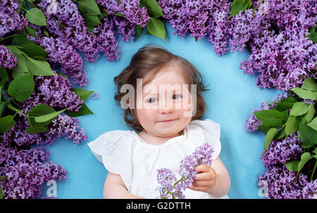 Jolie petite fille couchée sur fond bleu avec des fleurs lilas Banque D'Images
