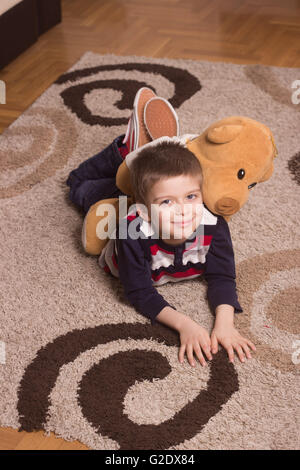 Young smiling boy portant sur plancher, tapis. Banque D'Images