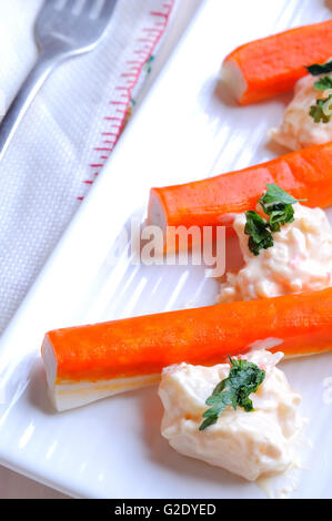 Bâtonnets de surimi avec de la sauce sur une assiette blanche sur une table en bois blanc Vue de dessus Banque D'Images