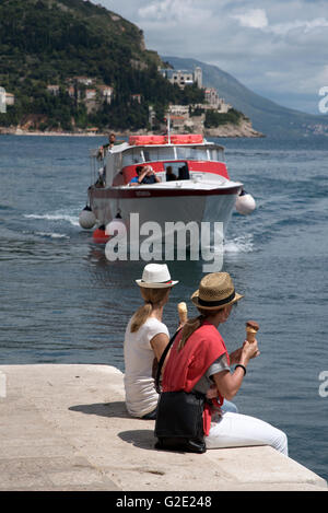 Le port de DUBROVNIK CROATIE Deux jeunes femmes touristes assis sur le mur du port de la vieille ville de Dubrovnik eating ice cream Banque D'Images