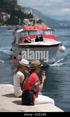 Le port de DUBROVNIK CROATIE Deux jeunes femmes touristes assis sur le mur du port de la vieille ville de Dubrovnik eating ice cream Banque D'Images