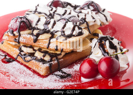 Gaufre Belge avec du sirop de chocolat et crème fouettée cerise rouge sur plaque rouge Banque D'Images