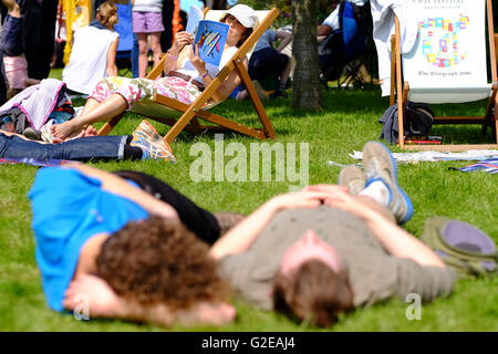 Hay-on-Wye, au Pays de Galles, Royaume-Uni. 29 mai, 2016. Une femme lit le visiteur du Festival programme alors qu'elle se détend dans une chaise longue sur la pelouse du Festival tandis que d'autres la répétition du Festival du gazon. Banque D'Images