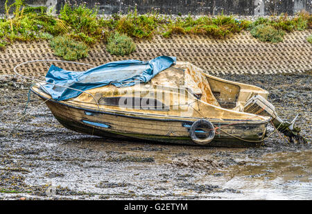 Apparemment abandonnée petite cabine cruiser étendu sur la vase à marée basse et à l'usure extrêmement pire pour Banque D'Images