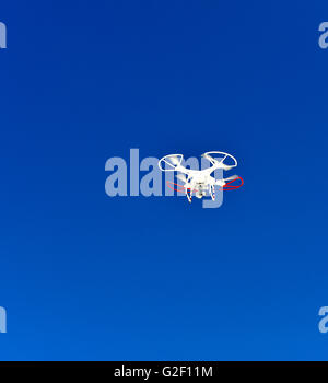 Un drone militaire vole au-dessus avec les pales du rotor rouge et bleu à l'extérieur contre un fond de ciel bleu vif Banque D'Images
