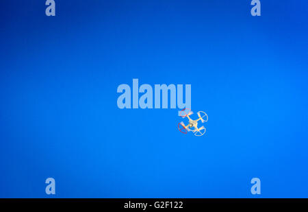 Un drone ou UAV vole au-dessus avec les pales du rotor rouge et bleu à l'extérieur contre un fond de ciel bleu vif Banque D'Images