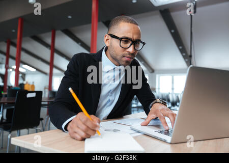 Les jeunes employés à la recherche d'ordinateur au concentré de surveiller et de noter au cours de la journée de travail à l'office de tourisme Banque D'Images