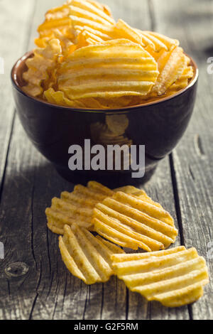 Croustilles de pommes de terre coupe ondulée sur table de cuisine. Croustilles de pommes de terre épicées savoureuses dans un bol. Banque D'Images