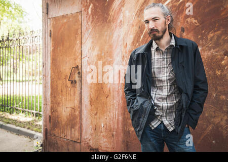 Portrait plein air de jeune homme asiatique barbu dans les tenues sur fond de mur garage grunge rouillé