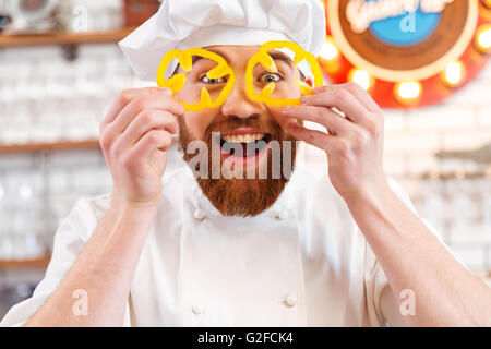 Cheerful amusant holding tranches de poivron jaune devant ses yeux Banque D'Images