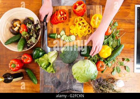 Vue de dessus de mains de jeune homme légumes frais de coupe sur table en bois Banque D'Images