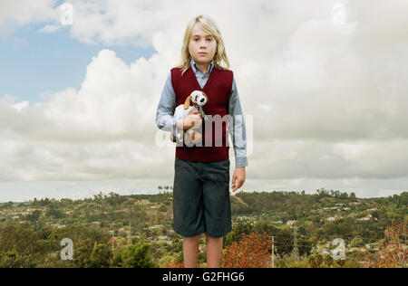 Jeune garçon avec de longs cheveux blonds Holding Stuffed Dog Banque D'Images