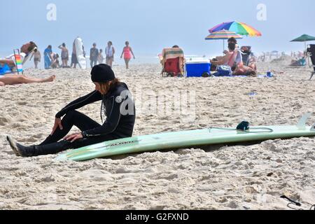 Une femme dans un wet suit assis sur la plage à côté de sa planche de surf Banque D'Images