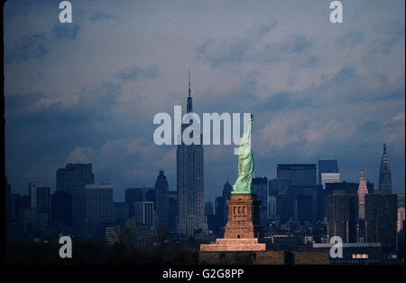 USA - New York. Bien allumé en statue de la liberté à l'Empire State Building à l'ombre, vue de Bayonne, New Jersey Banque D'Images