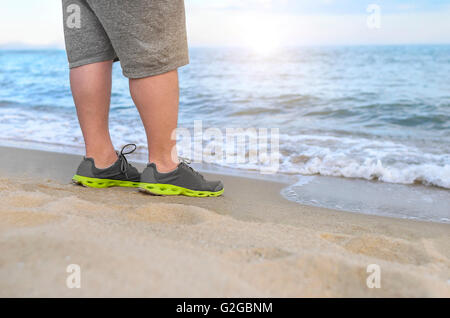 L'homme se dresse sur la plage. Les pieds dans des chaussures de course libre. Banque D'Images