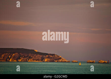 Petit yacht arrondir les aiguilles au large de l'île de Wight dans la lumière du soir Banque D'Images