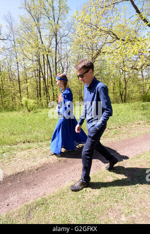 Jeune fille russe en costume bleu traditionnel de la Russie et un jeune garçon marchant sur un chemin à travers une forêt Banque D'Images