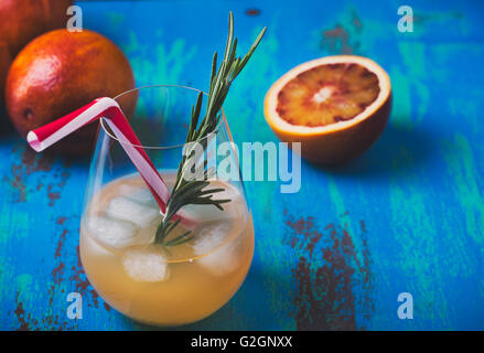 Jus frais pressé et orange sanguine sur fond bleu, la tequila palomas avec romarin, boisson d'été Banque D'Images