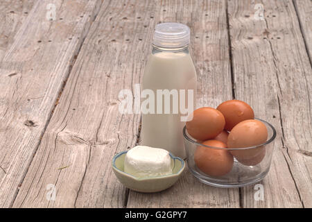 Brown bio frais oeufs dans un bol en verre clair, verre bouteille de lait et fromage de chèvre sur une ferme rustique table de pique-nique en été. Banque D'Images