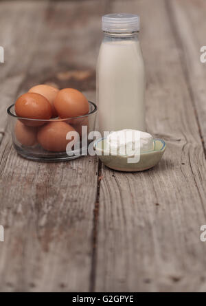 Brown bio frais oeufs dans un bol en verre clair, verre bouteille de lait et fromage de chèvre sur une ferme rustique table de pique-nique en été. Banque D'Images