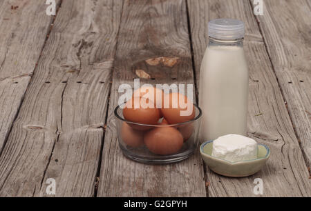 Brown bio frais oeufs dans un bol en verre clair, verre bouteille de lait et fromage de chèvre sur une ferme rustique table de pique-nique en été. Banque D'Images