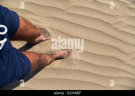 Les jambes d'un homme marchant et laissant imprimer des pieds sur le sable Banque D'Images