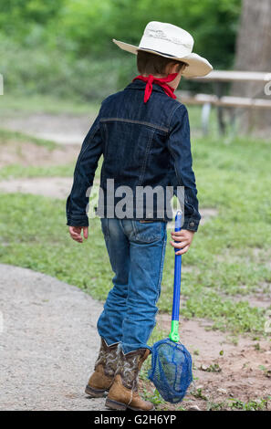 Un jeune garçon en tenue de cow-boy la collecte des grenouilles et des insectes à McKinney Falls State Park, Austin, Texas. USA. Banque D'Images