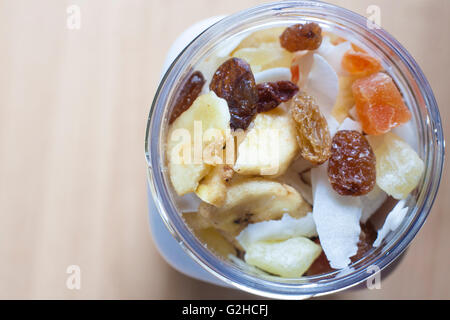 Pot en plastique avec un mélange de fruits secs sur la surface en bois. Focus sélectif. High angle view Banque D'Images