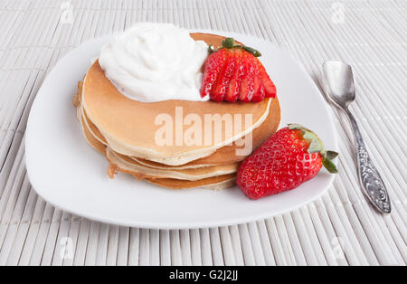 Des crêpes sur fond blanc avec de la crème de fraise et cuillère en argent Banque D'Images