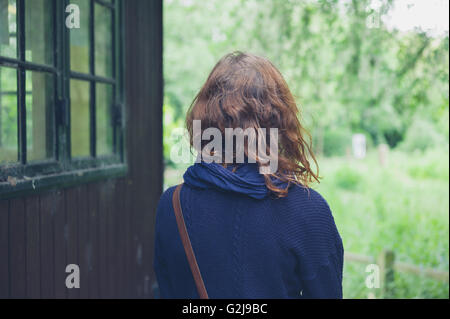 Une jeune femme se tient debout à l'extérieur par une cabane dans les bois Banque D'Images