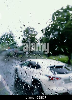 Vus blanc pendant la conduite en ville sous la pluie de derrière un verre couvert de gouttes de pluie Banque D'Images