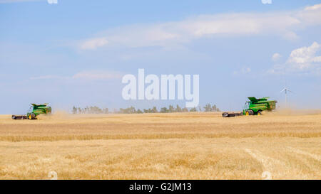 Deux moissonneuses-batteuses John Deere récoltes de blé dans l'Oklahoma, USA. En arrière-plan de l'éolienne. Banque D'Images