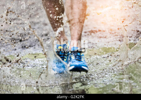 Trail Runner homme marchant dans une flaque d'eau, éclaboussant ses chaussures. Sentier de ski de fond Banque D'Images