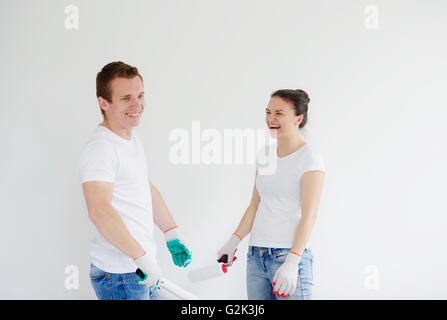 Jeune homme et la femme rire, d'entreprendre la réparation. Sur les mains des gants. Ils détiennent de rouleaux pour la peinture. Couple de bonne humeur Banque D'Images