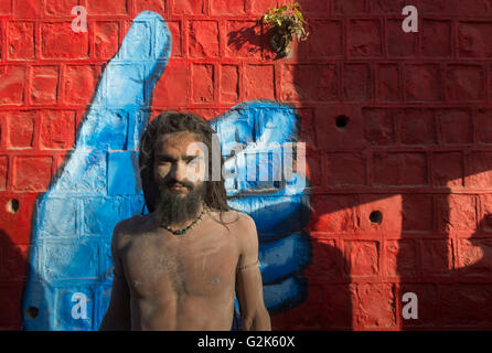 Naga Sadhu en face de la main bleu peint sur mur de brique rouge à la rivière Shipra Ghats, Shahi Snaan (Royal Immersion Sainte), Ujjain K Banque D'Images